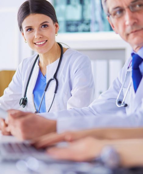 Smiling doctor using a laptop working with her colleagues in a bright hospital room